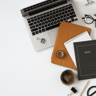 A laptop, notebooks and stationery laid out on a white desk