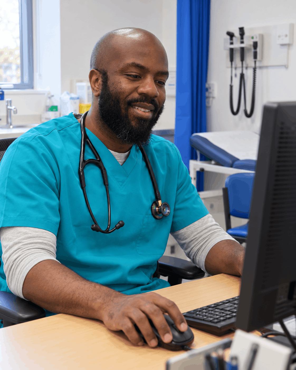 Chris in clinic, working at a computer in his scrubs